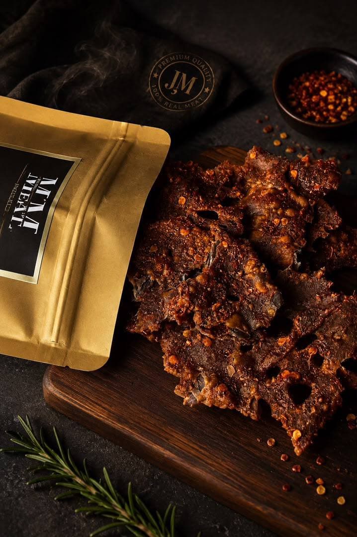 A gloved hand holding a torn, chili-flecked slab of kilishi